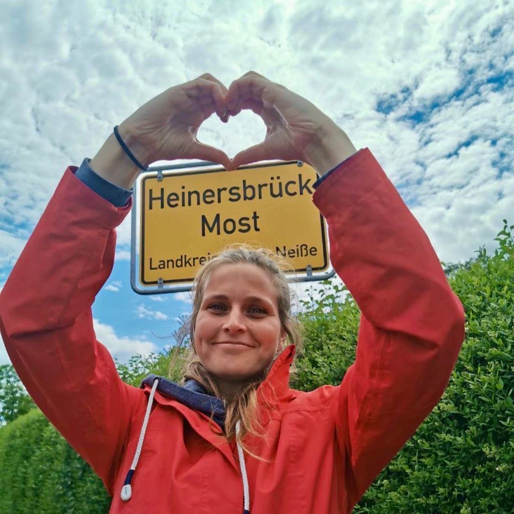 Frau Wallstein steht vor dem Ortsschild der Gemeinde Heinersbrück Most.